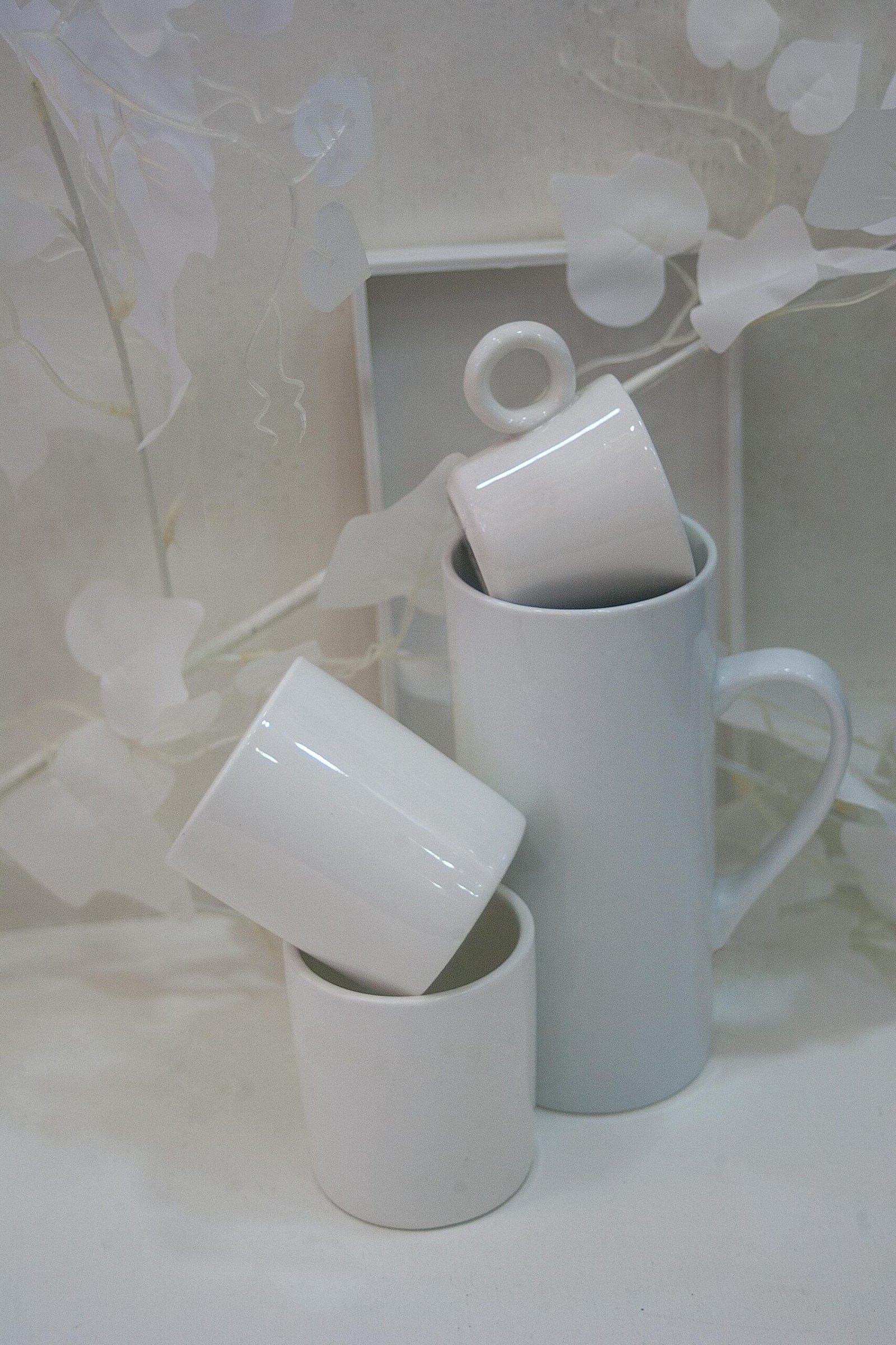 A minimalist still life of stacked white ceramic cups against a soft background.